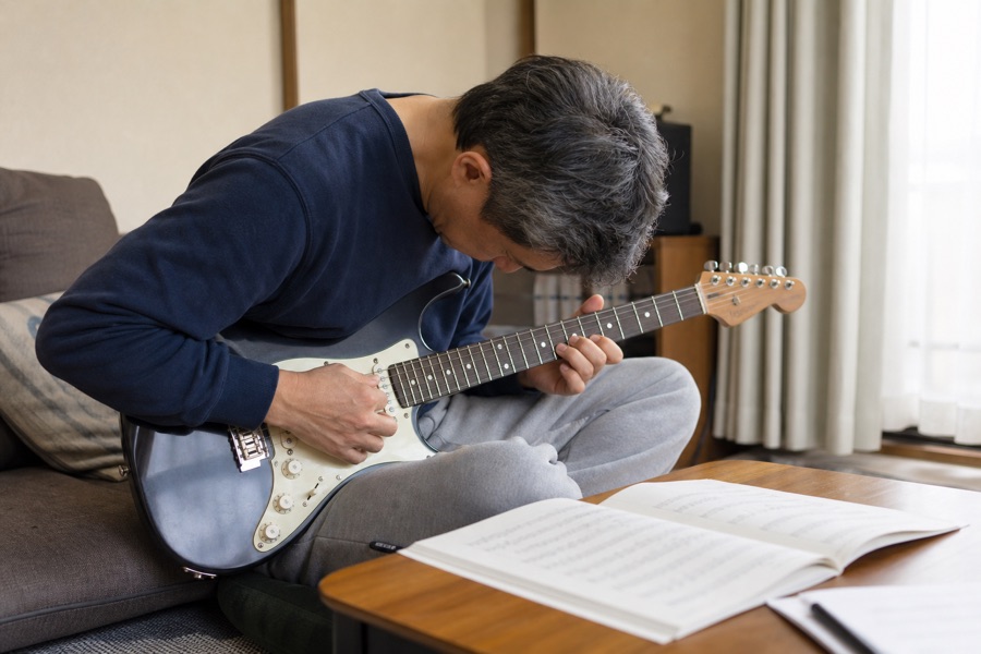 背中を丸めてギターを覗き込む中年男性